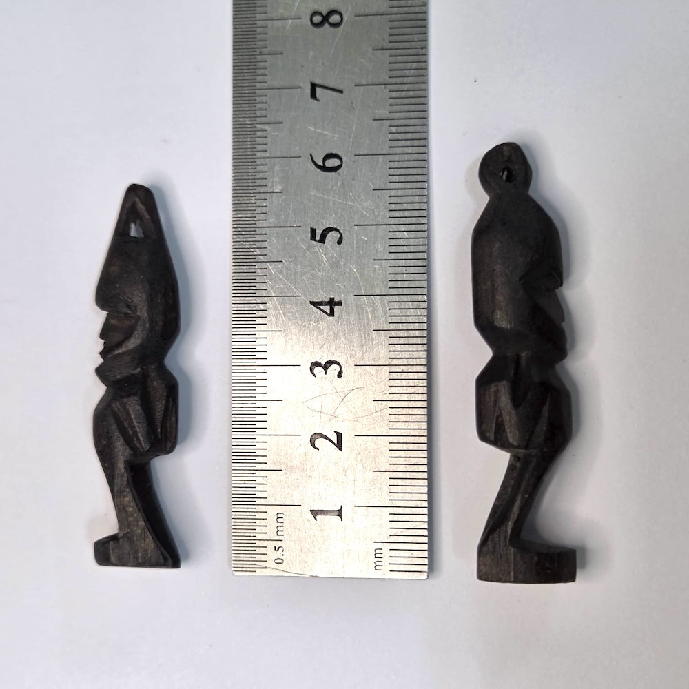 Two black african vintage wooden figures on a white background next to a ruler to show scale