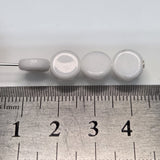 Close-up of white flat round beads with a glossy finish next to a ruler to show size