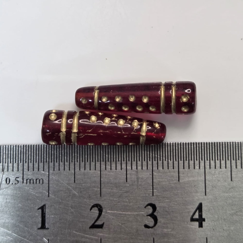 Two red cylindrical beads with gold accents on a ruler for scale.