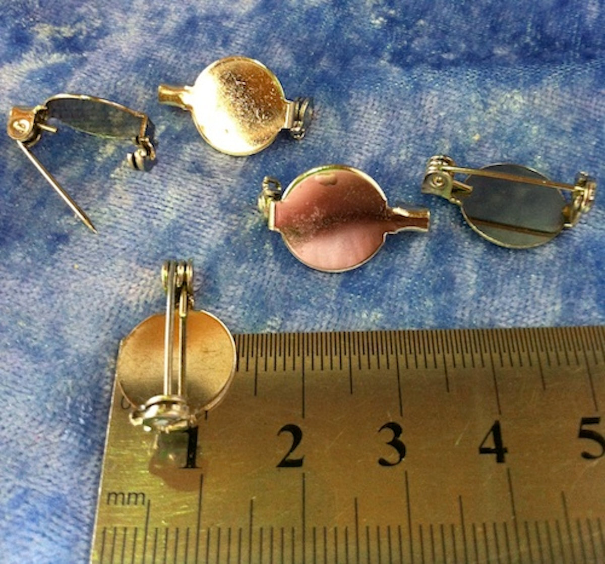 nickel silver brooches on a blue fabric background with a ruler for scale.