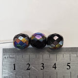Three faceted beads of different colors on a ruler for scale.