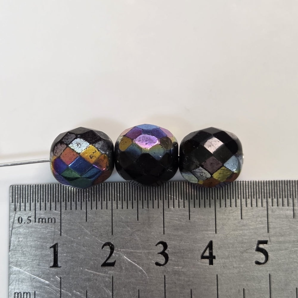 Three faceted beads of different colors on a ruler for scale.