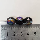 Three faceted beads of different colors on a ruler for scale.