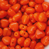 A close-up image of small orange Czech glass hearts beads with holes showing, intended for crafting and jewelry making.