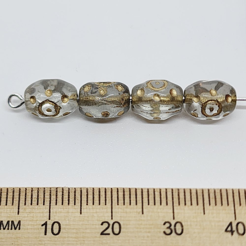 A close-up image of small, clear oval-shaped Czech glass beads with gold accents threaded on a pin to show the direction of the hole