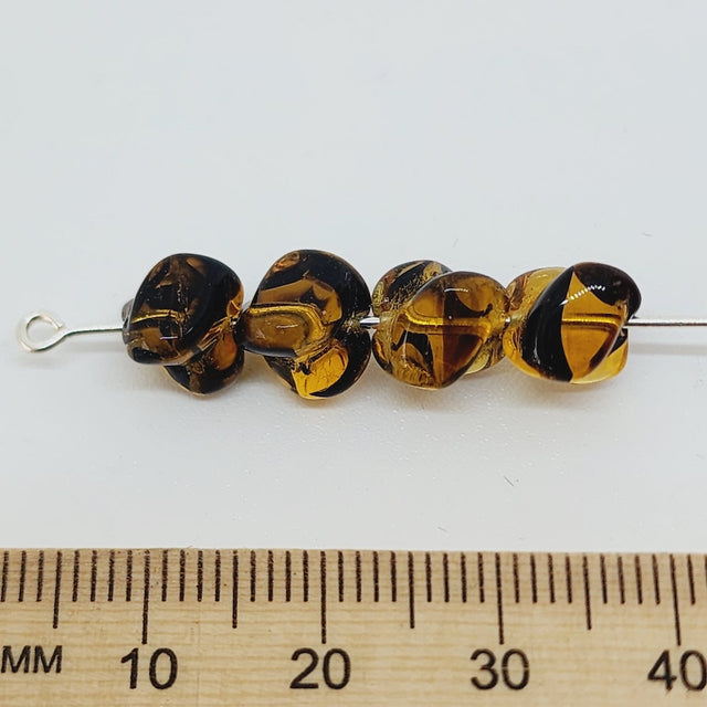 tortoise shell style beads on a pin on a white background with a ruler for scale