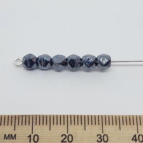 gunmetal grey facet beads on a pin with a ruler to show scale