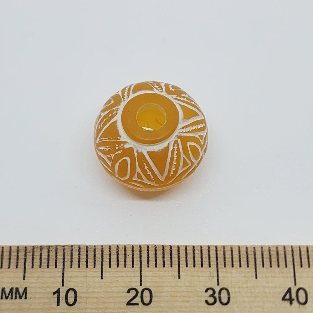 A collection of vintage orange and white baroque-patterned lucite beads with a white line bordering each bead against a ruler to show scale