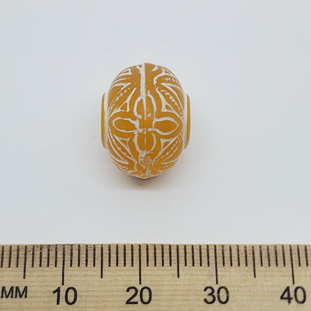 A collection of vintage orange and white baroque-patterned lucite beads with a white line bordering each bead against a ruler to show scale