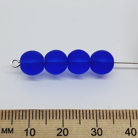 four dark blue matte beads with a ruler to show scale