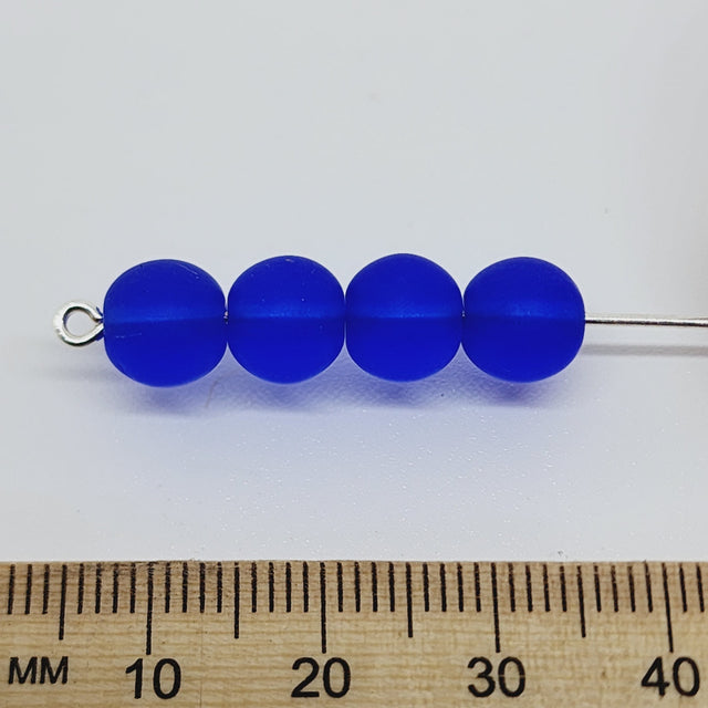 four dark blue matte beads with a ruler to show scale