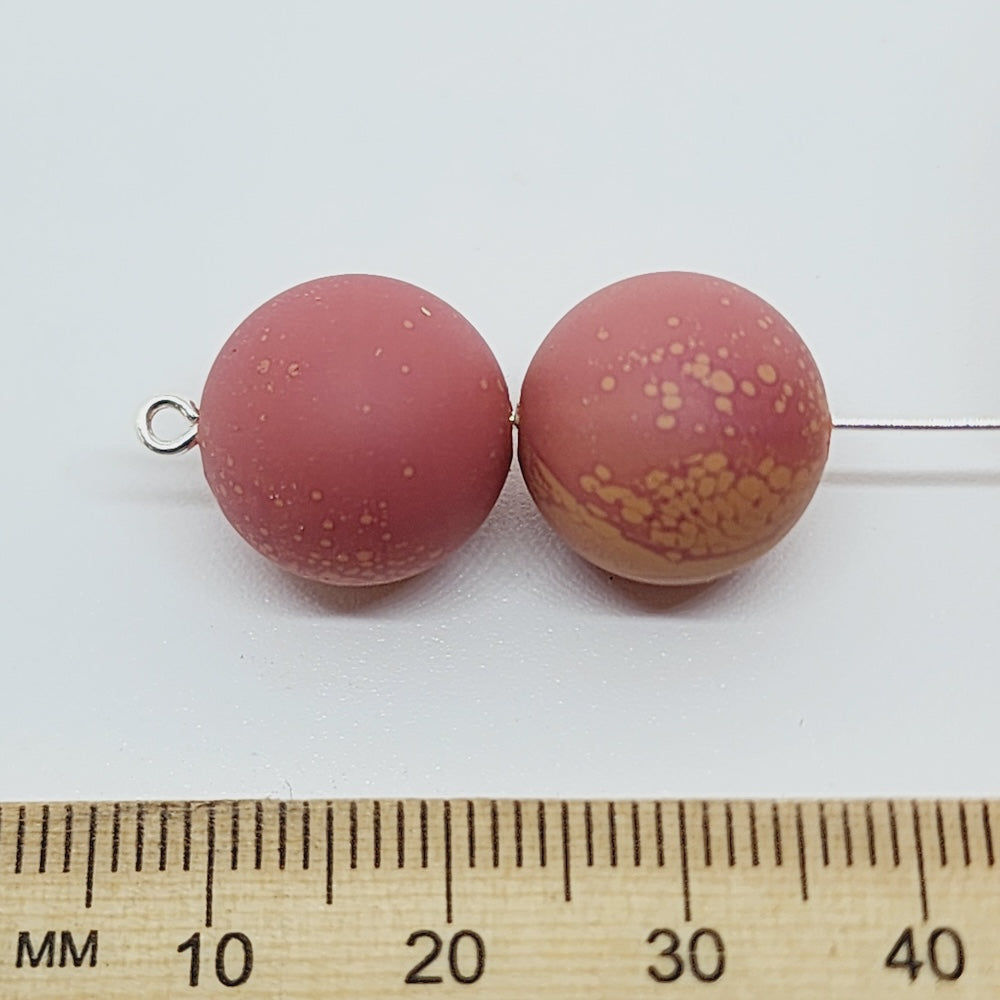 Two rust brown speckled beads on a white background with a ruler for scale.