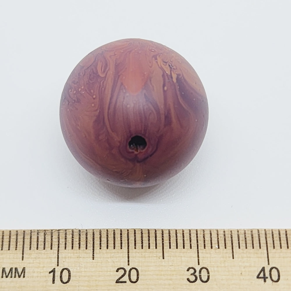 Marbled brown bead with a ruler for scale on a white background