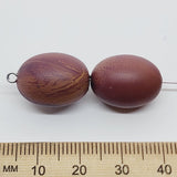 Two brown beads next to a ruler on a white background
