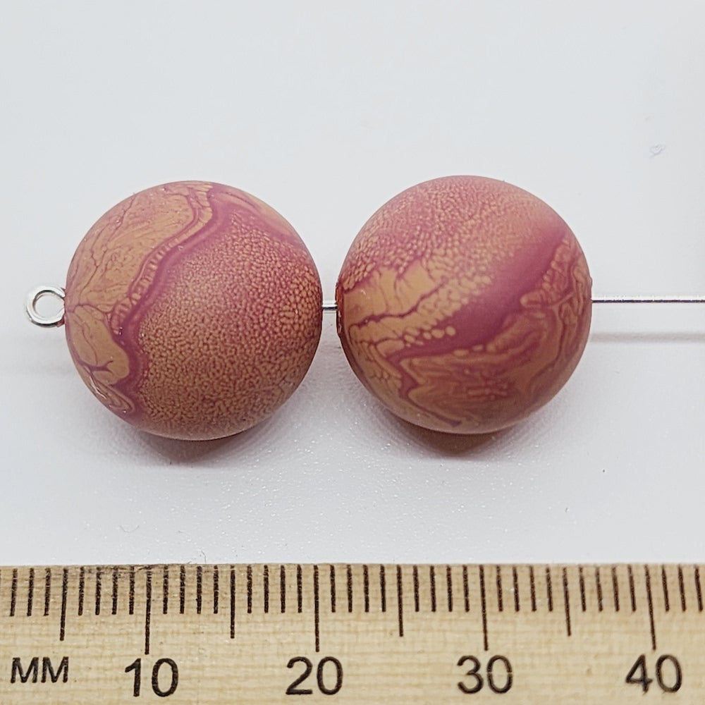 Two marbled brown beads with a ruler for scale on a white background
