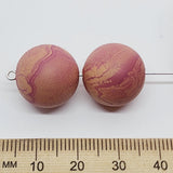 Two marbled brown beads with a ruler for scale on a white background