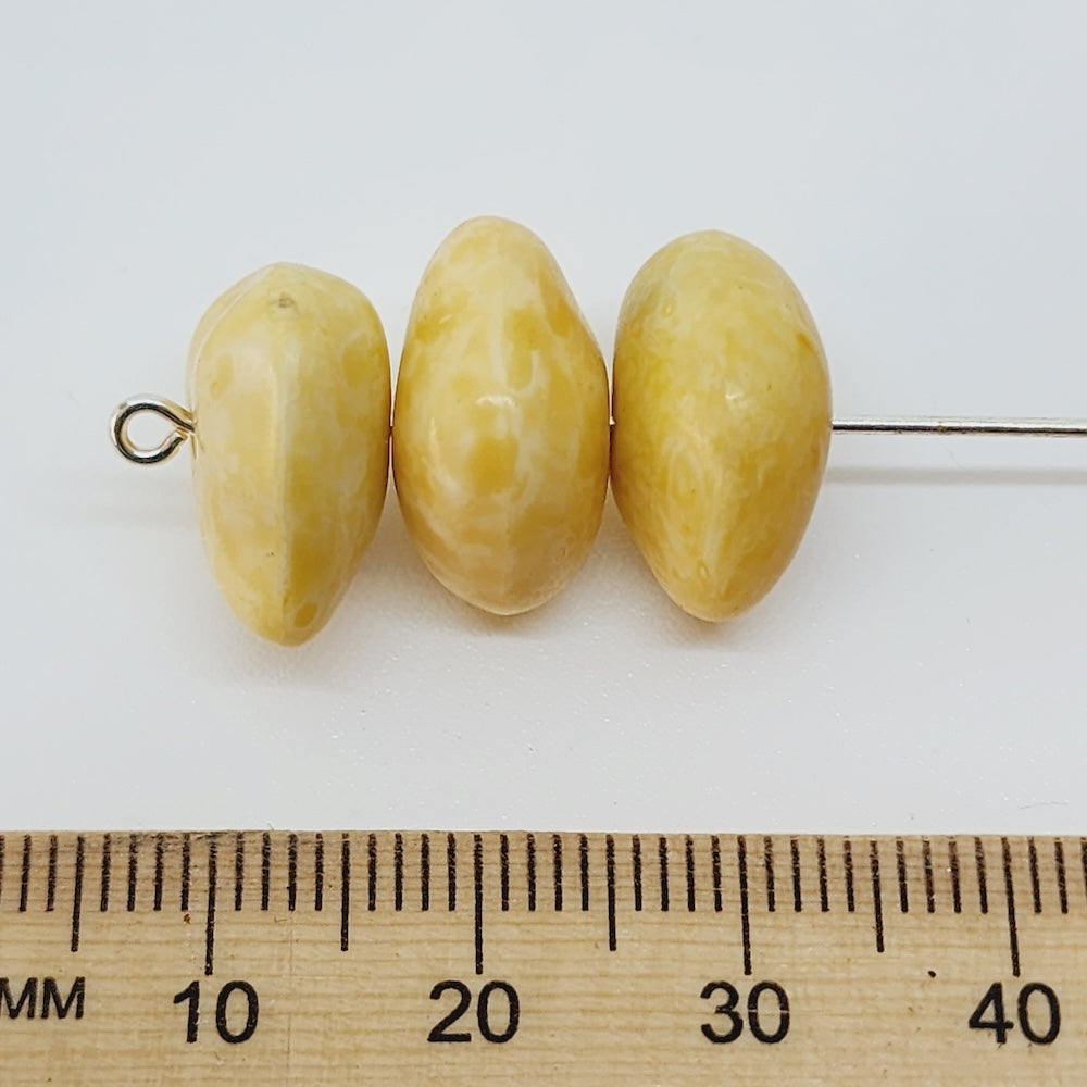 Three yellow beads on a stick with a ruler below for scale on a white background