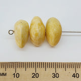 Three yellow beads on a stick with a ruler below for scale on a white background