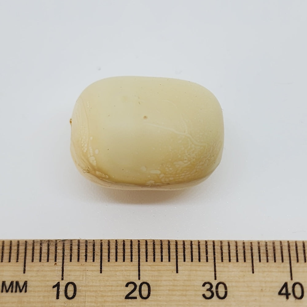 Beige barrel shape bead next to a wooden ruler on a white background