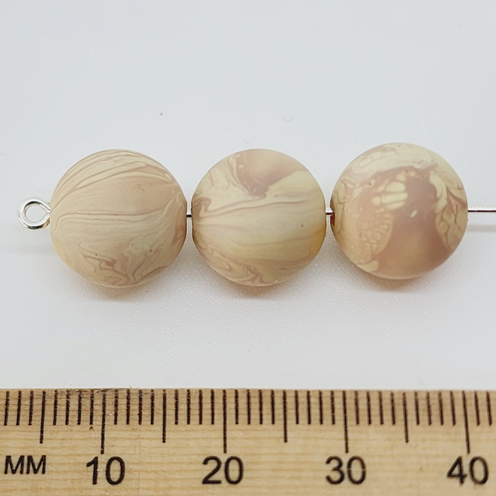 Three marbled beige beads on a white background with a wooden ruler for scale.