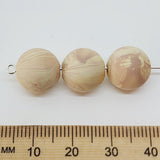 Three marbled beige beads on a white background with a wooden ruler for scale.