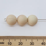 Three beige beads on a white background with a wooden ruler for scale.