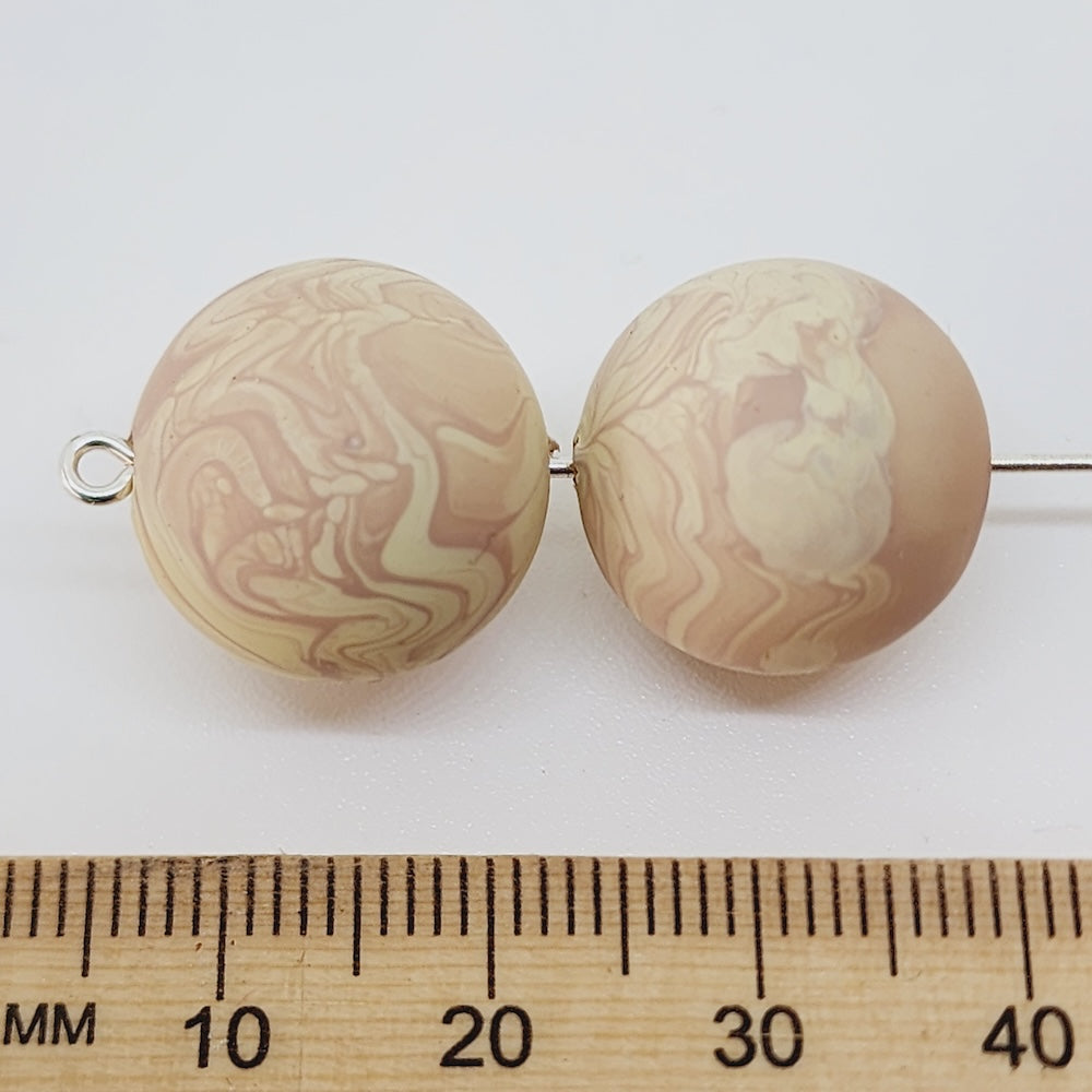 Two marbled beige beads on a white background, next to a wooden ruler for scale.