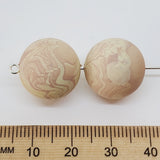 Two marbled beige beads on a white background, next to a wooden ruler for scale.