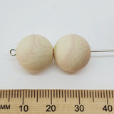 Two marbled acrylic beads with a ruler for scale on a white background