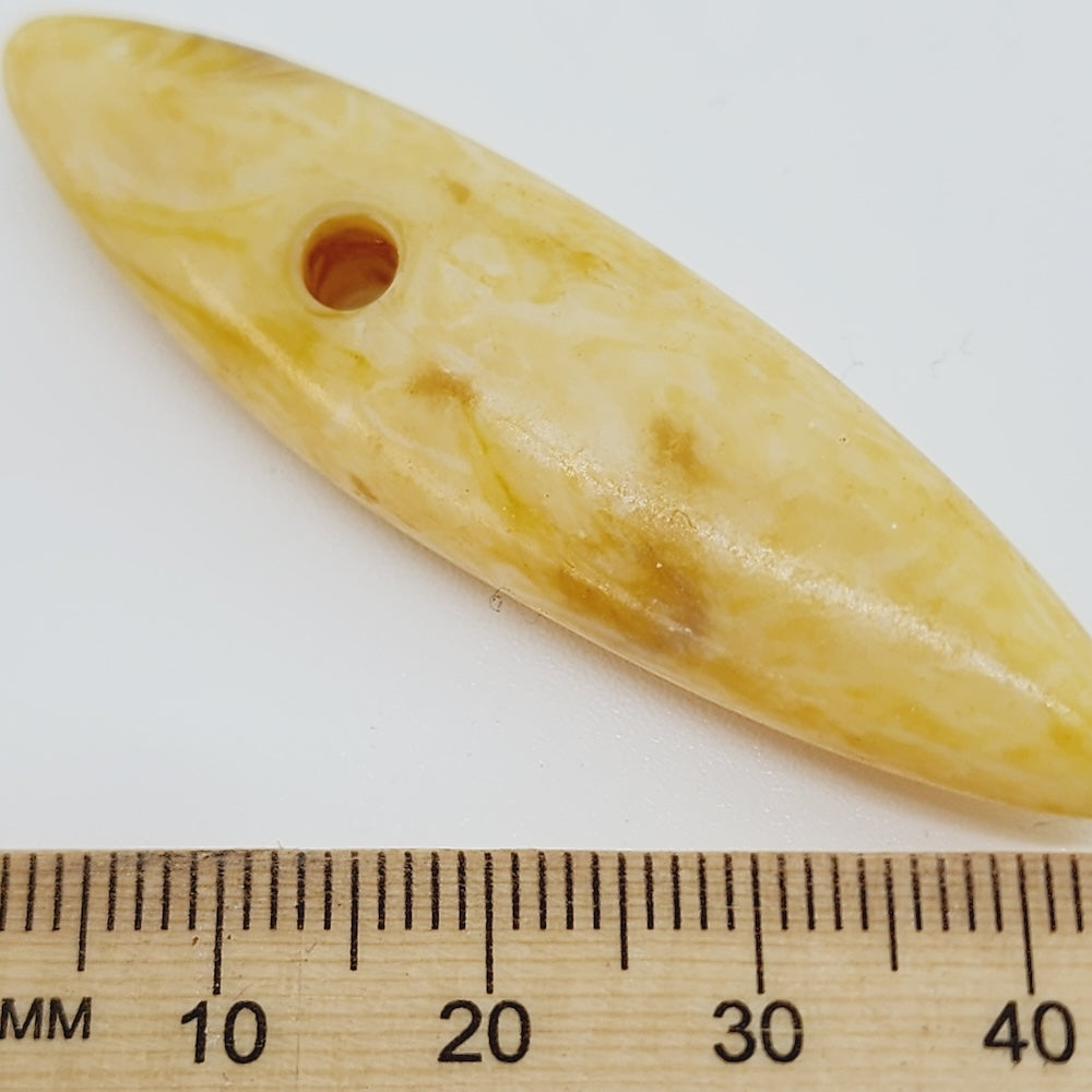 Cream spear shape bead with a large hole on a white background, next to a wooden ruler for scale.