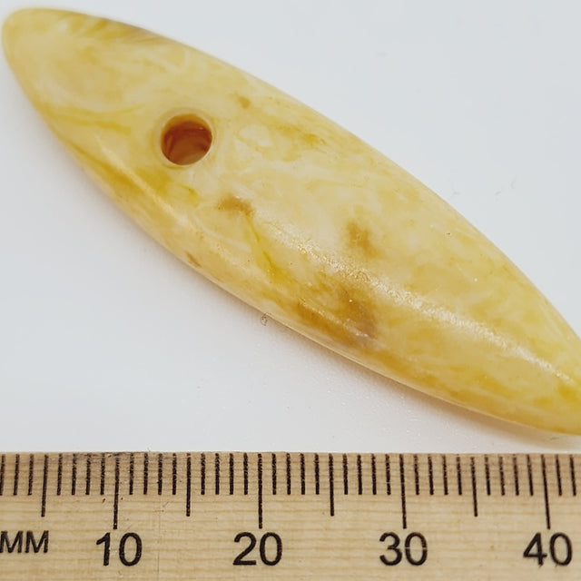 Cream spear shape bead with a large hole on a white background, next to a wooden ruler for scale.