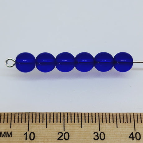 dark blue round glass beads on a pin with a ruler to show scale