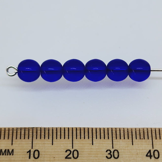 dark blue round glass beads on a pin with a ruler to show scale
