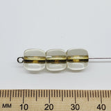 Three clear beads with green stripes on a white background with a ruler for scale.