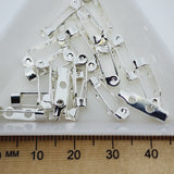 silver brooch backs displayed in a white dish with a wooden ruler for scale