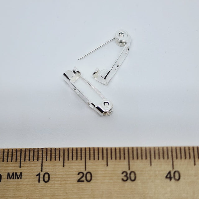 Silver brooch pin on a white background with a wooden ruler for scale.