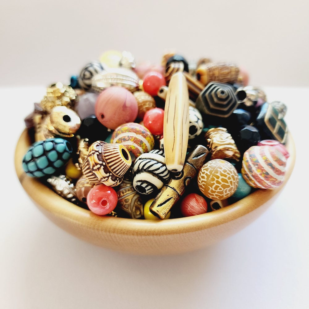 A collection of colorful, intricately patterned vintage craft beads in a small wooden bowl on a white surface.