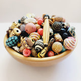 A collection of colorful, intricately patterned vintage craft beads in a small wooden bowl on a white surface.