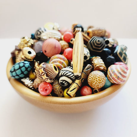 A collection of colorful, intricately patterned vintage craft beads in a small wooden bowl on a white surface.
