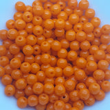 Opaque orange round beads in a group on a white background