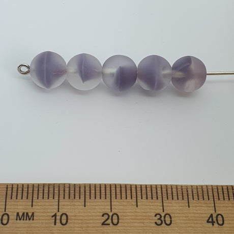 A collection of round, clear glass beads with a milky purple tint on a pin with a ruler for scale