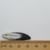 Feather-shaped bead with black and white design on a white background, measured against a ruler.