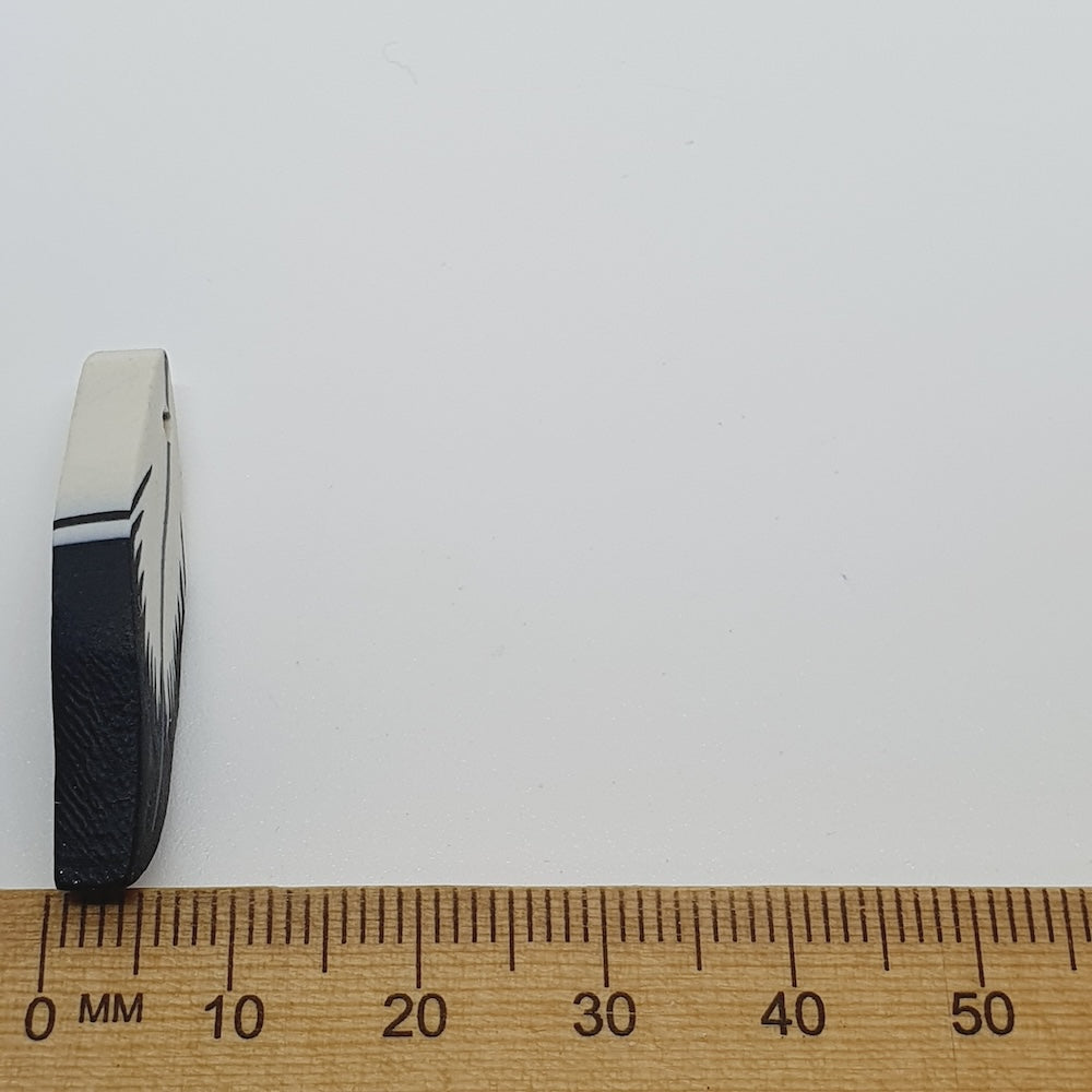 feather bead next to a wooden ruler on a white background
