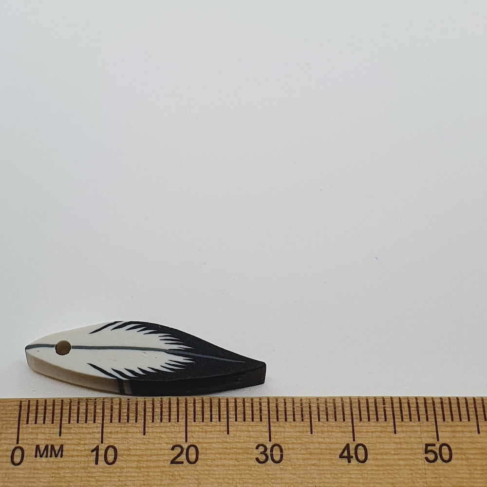 Small feather-shaped bead next to a wooden ruler on a white background