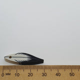 Small feather-shaped bead next to a wooden ruler on a white background