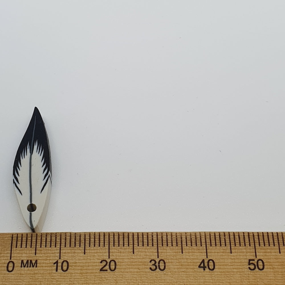 Small feather-shaped bead next to a wooden ruler on a white background