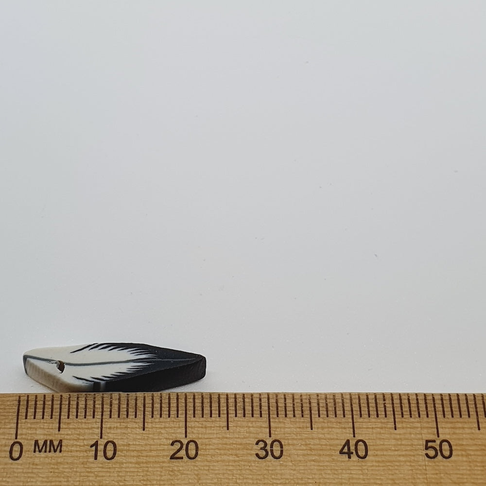 Small black and white feather bead next to a wooden ruler on a white background