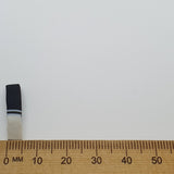 side on photos of a feather bead with black and white bands on a wooden ruler against a white background