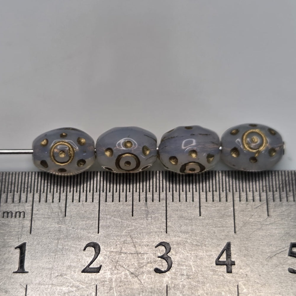 Four clear beads with metallic patterns with threading on a metal ruler for scale.