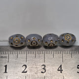 Four clear beads with metallic patterns with threading on a metal ruler for scale.